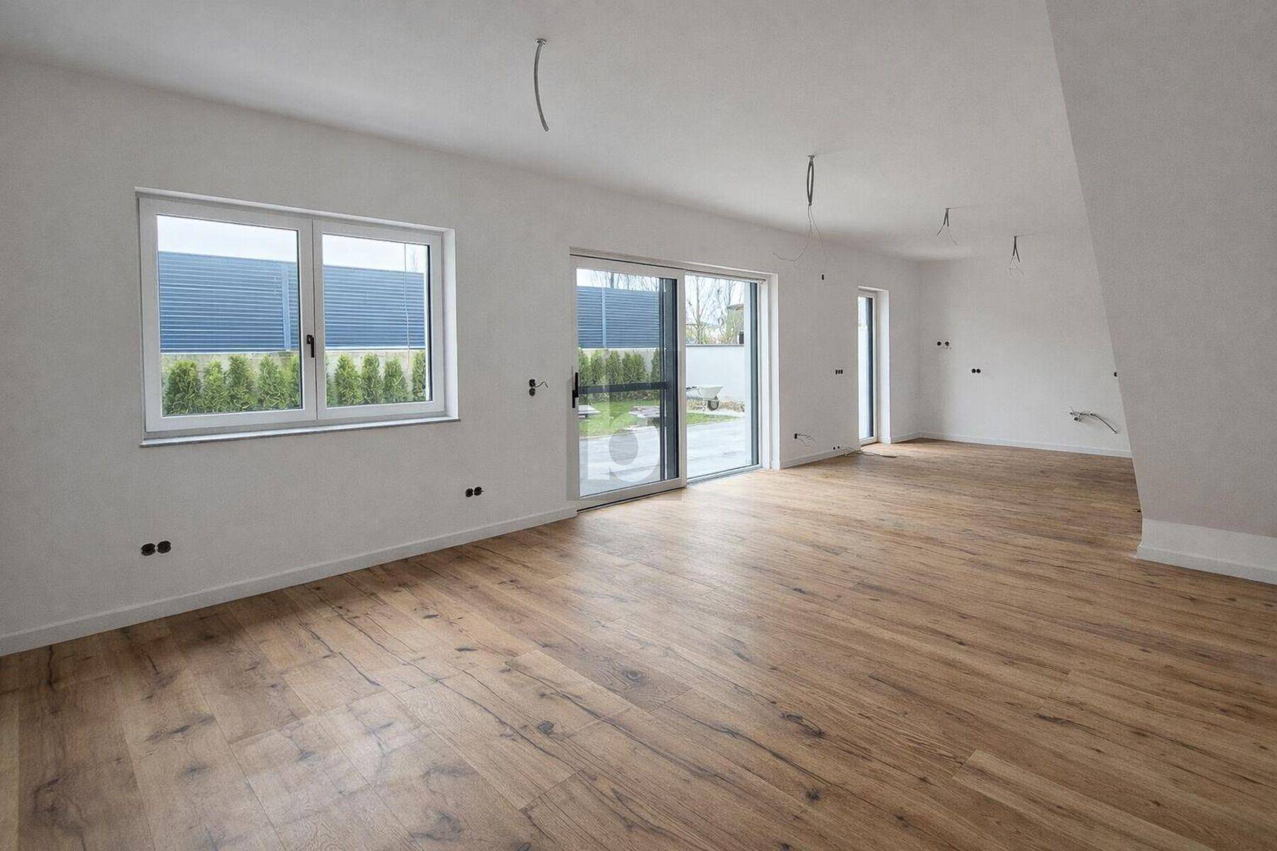 Heller, unmöblierter Wohnraum mit Holzboden und großen Fenstern zum Garten.