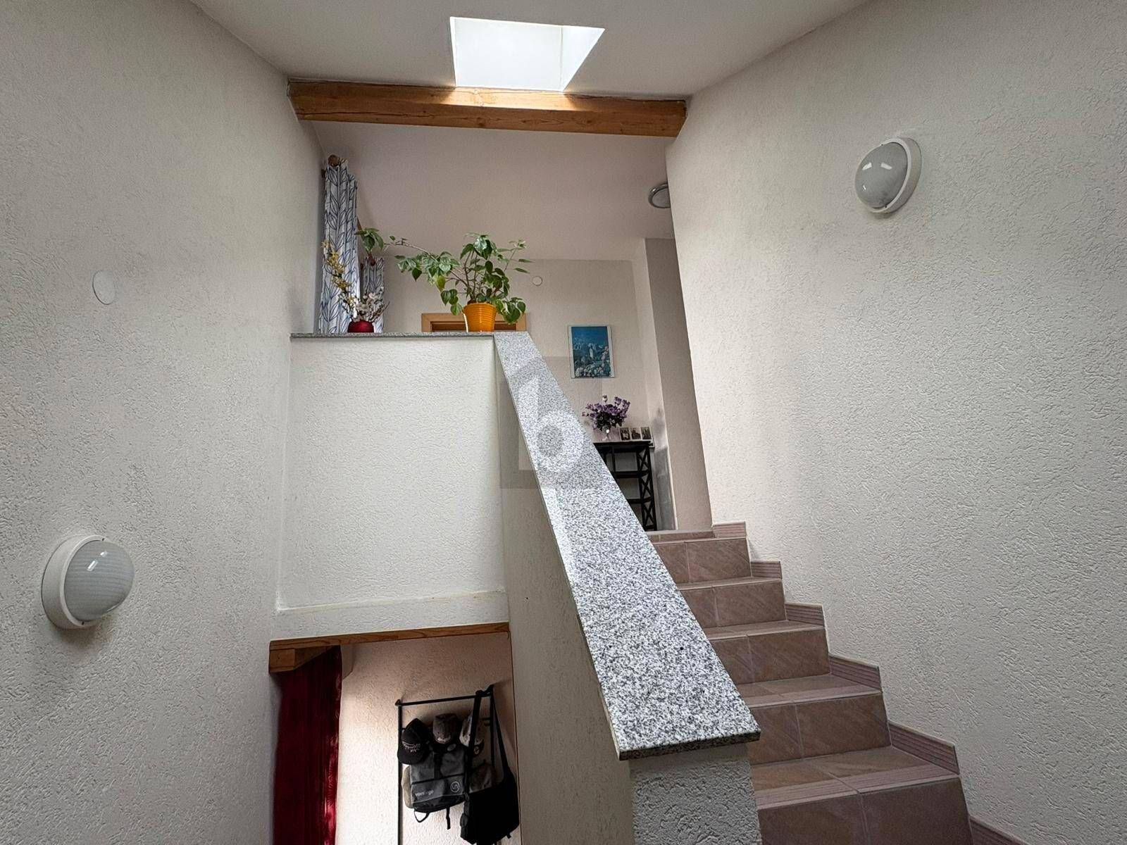 Helles Treppenhaus mit Granitstufen, Holzdetails und natürlichem Licht durch ein Dachfenster.