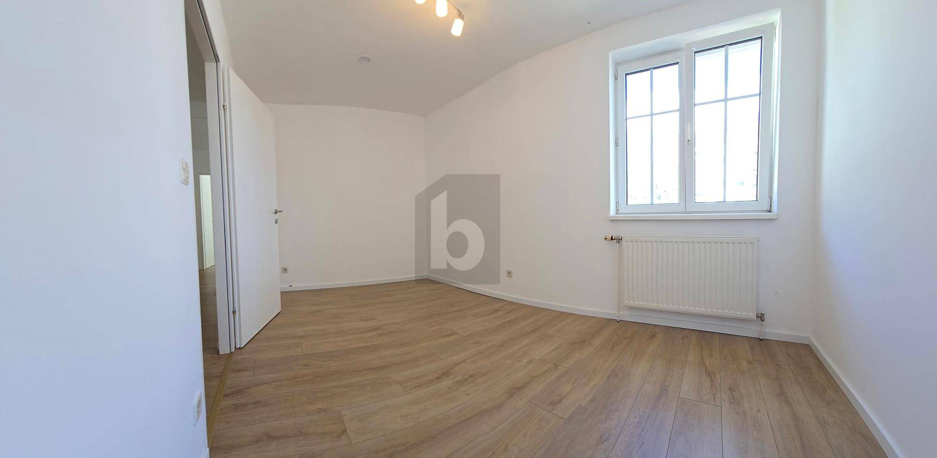 Helles Schlafzimmer mit Laminatboden, weißen Wänden und einem großen Fenster.