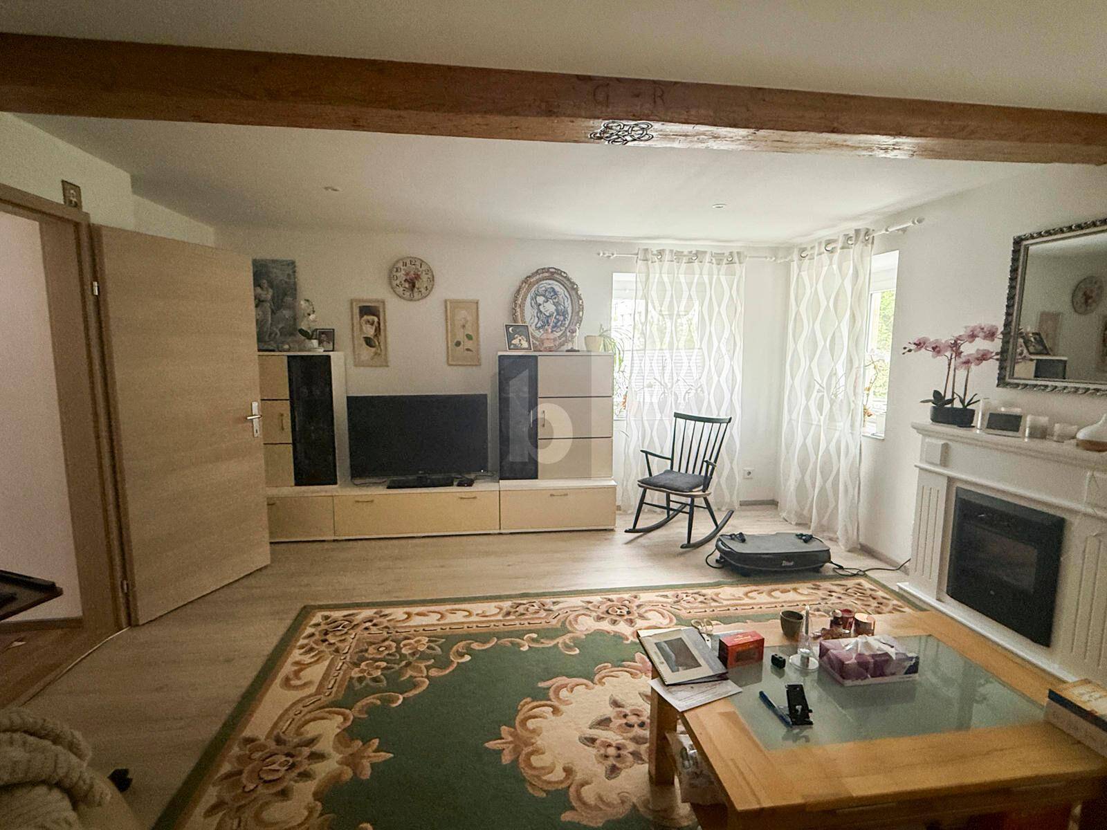 Gemütliches Wohnzimmer mit Kamin, Fernsehmöbeln, Teppich und einem sichtbaren Holzbalken.
