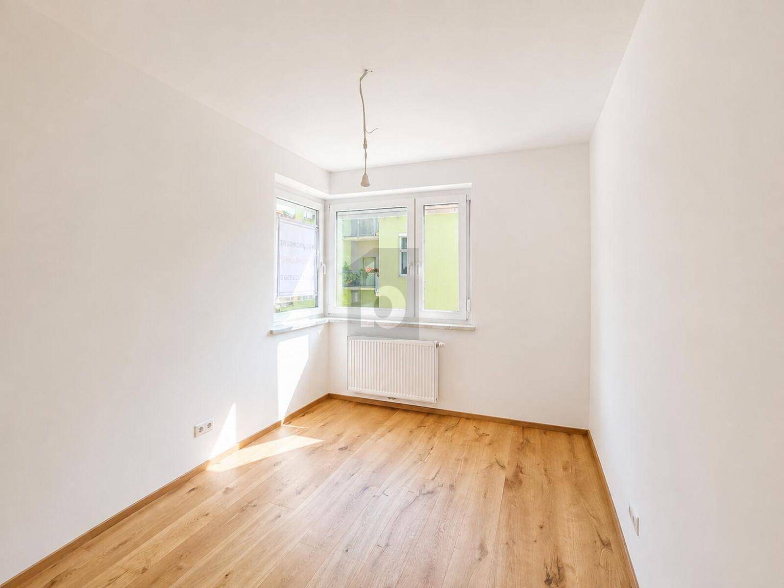 Geräumiges Zimmer mit großen Fenstern und Holzboden, ideal für Schlaf- oder Wohnbereich.