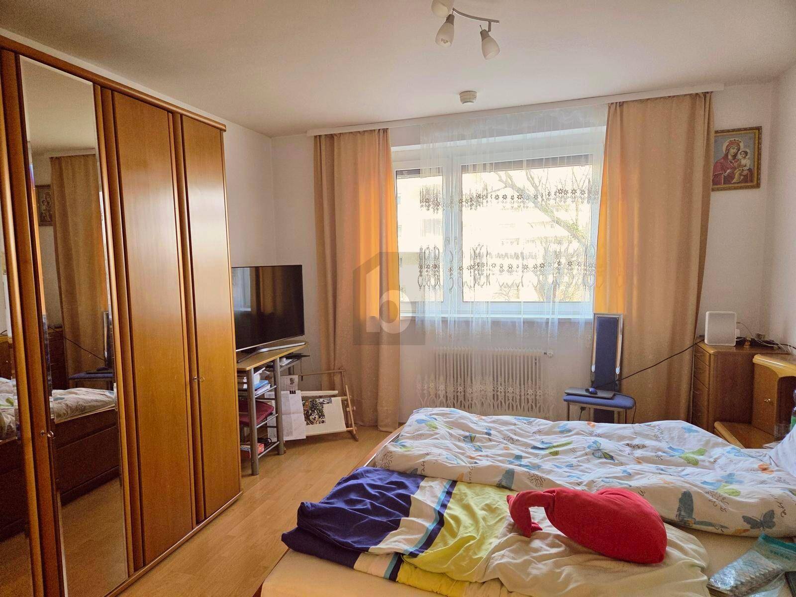 Gemütliches Schlafzimmer mit großem Bett, Holzschrank mit Spiegeltüren und Fenster für natürliches Licht.