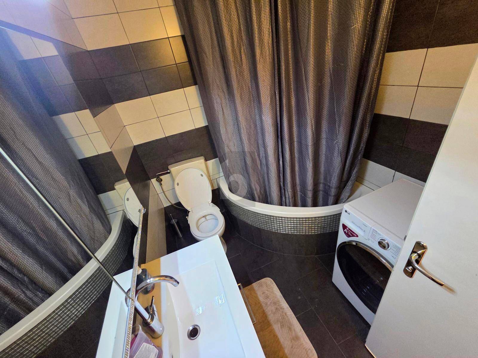 Badezimmer mit schwarz-weißen Fliesen, Toilette, Waschbecken, Dusch-Badewanne und Waschmaschine.