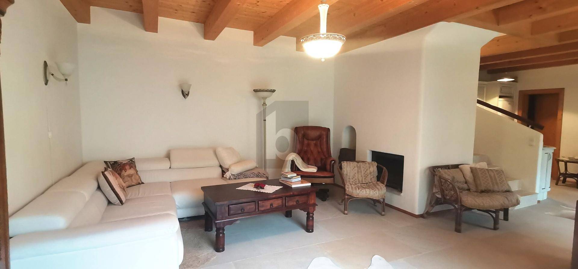 Gemütliches Wohnzimmer mit großem Ecksofa, Holzbalkendecke und einem integrierten Kamin.