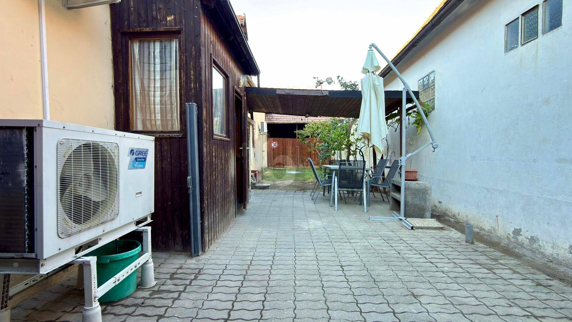 Gepflasterter Außenbereich mit Sitzgelegenheiten, Sonnenschirm und einer Klimaanlage an der Hauswand.