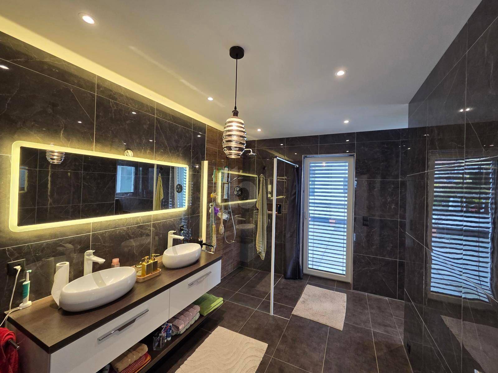 Modernes Badezimmer mit doppelten Waschbecken, großer begehbarer Dusche und dunklen Marmorfliesen.
