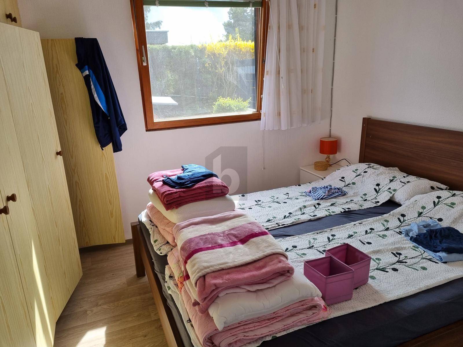 Gemütliches Schlafzimmer mit Holzbett, Kleiderschrank und einem Fenster mit Blick ins Grüne.