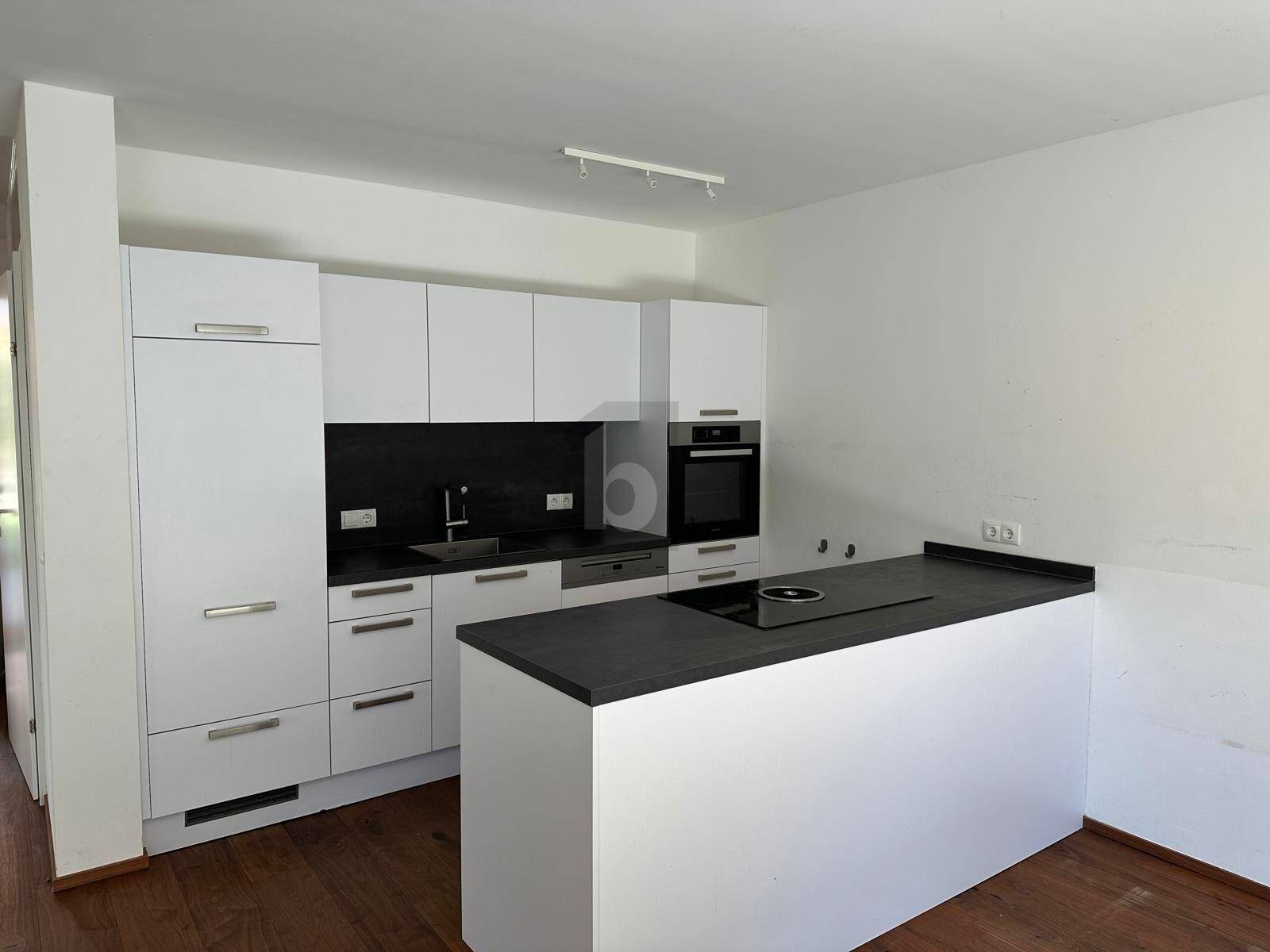 Moderne Einbauküche in Weiß mit dunkler Arbeitsplatte und integrierten Geräten.