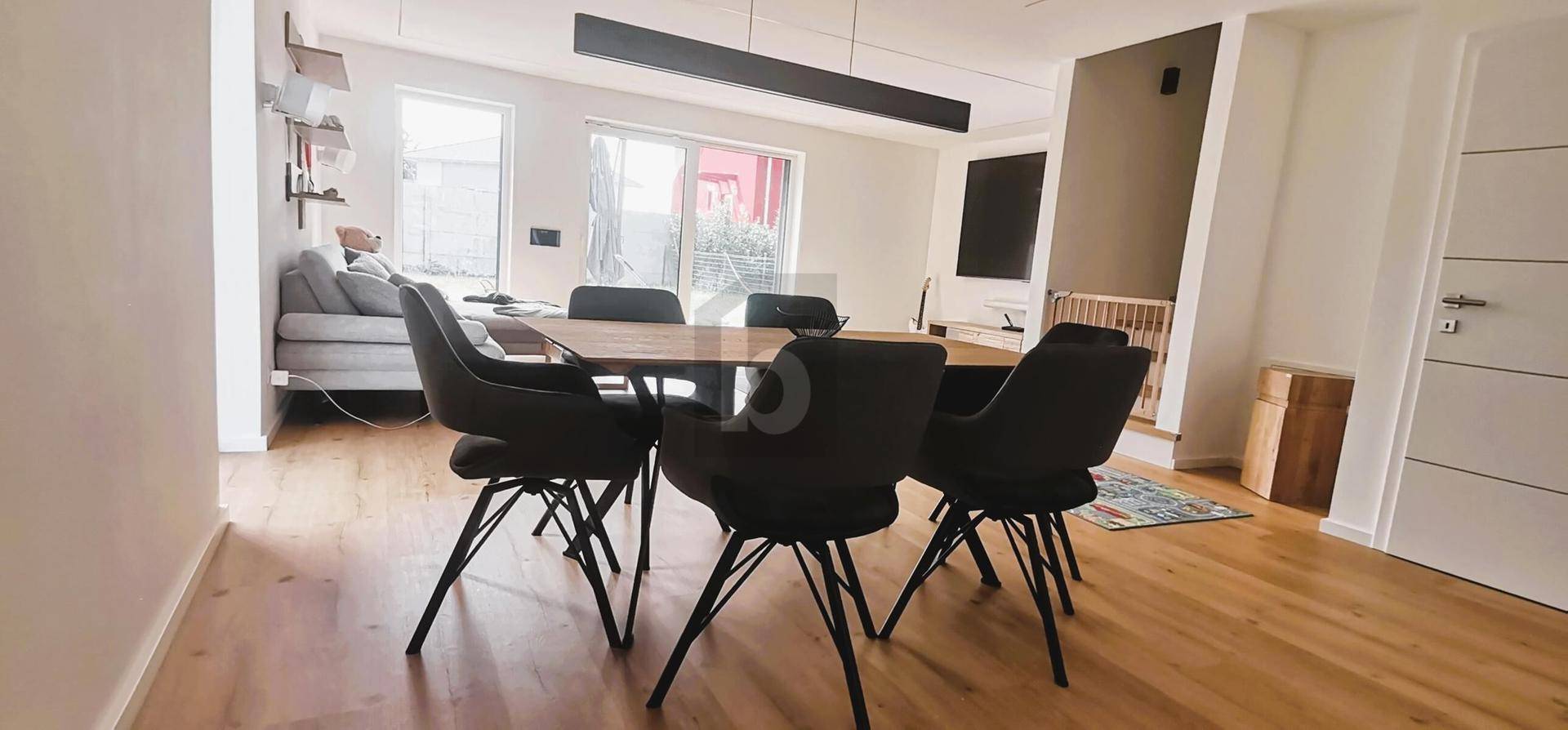 Moderner Essbereich mit Holztisch und schwarzen Stühlen, angrenzend an den Wohnbereich mit großen Fenstern.