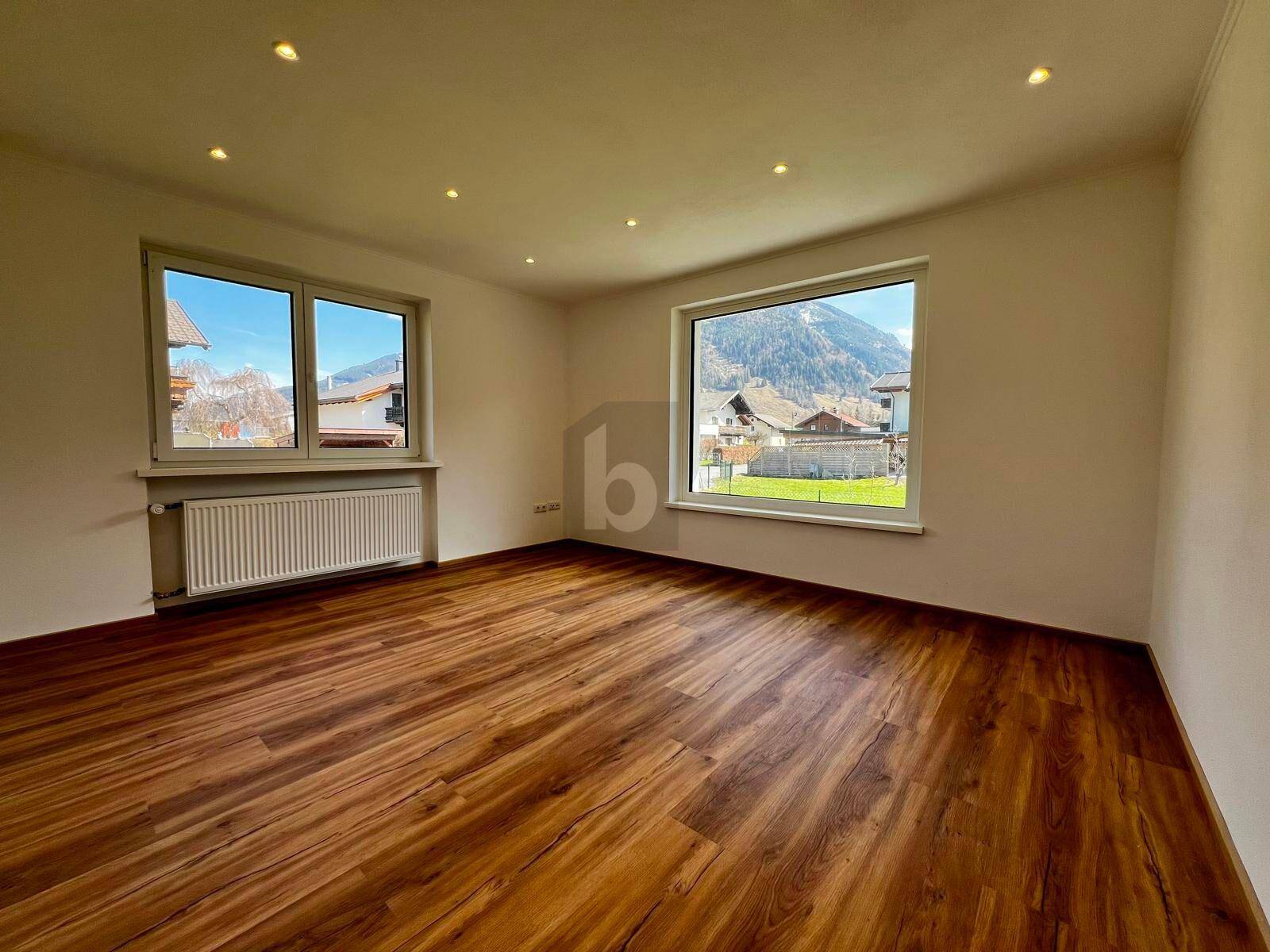 Geräumiger Innenraum mit Holzboden, weißen Wänden und weitem Blick auf die Berge.
