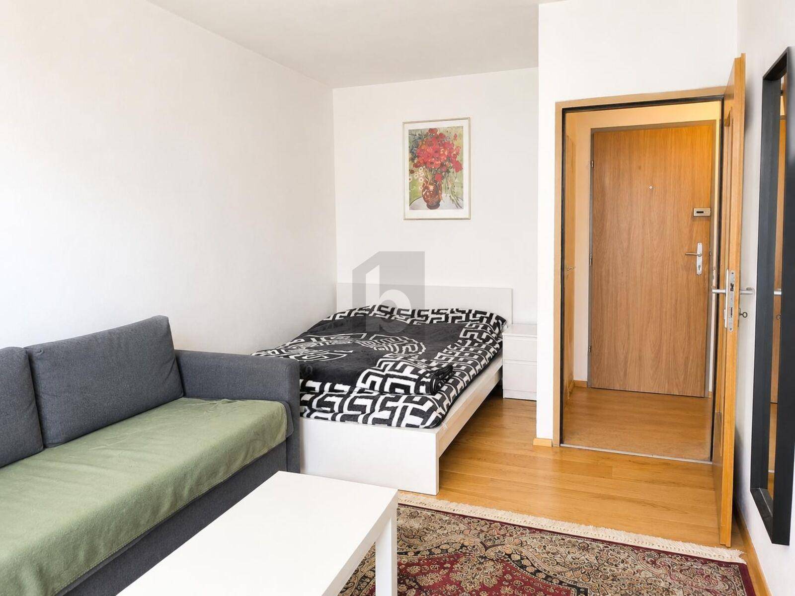 Schlafzimmer mit Bett, Sofa und Holzboden, direkt neben dem Eingangsbereich.