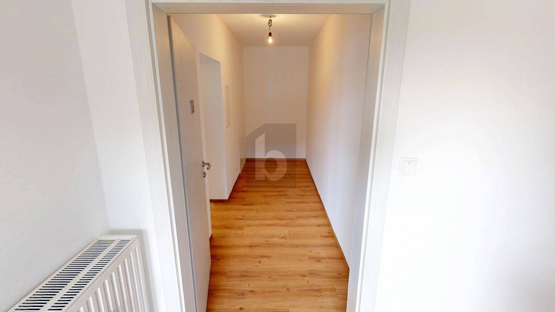 Schmaler Flur mit Holzboden und weiß gestrichenen Wänden, ausgestattet mit einem Heizkörper.