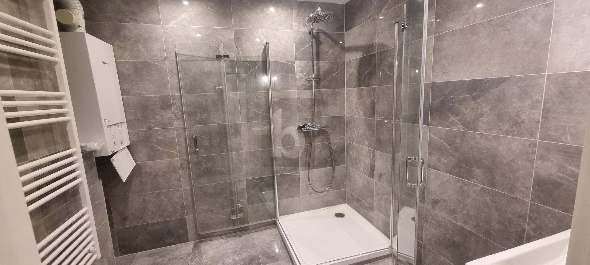 Modernes Badezimmer mit großer Duschkabine, grauen Fliesen und einem praktischen Handtuchheizkörper.