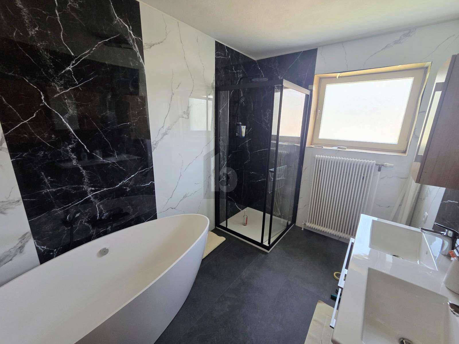 Modernes Badezimmer mit schwarz-weiß gemusterten Fliesen, einer freistehenden Badewanne und einer Duschkabine.