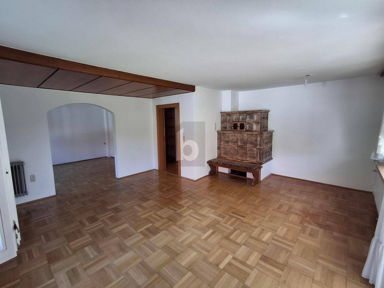 Geräumiges Wohnzimmer mit traditionellem Kachelofen, Parkettboden und weiß gestrichenen Wänden.