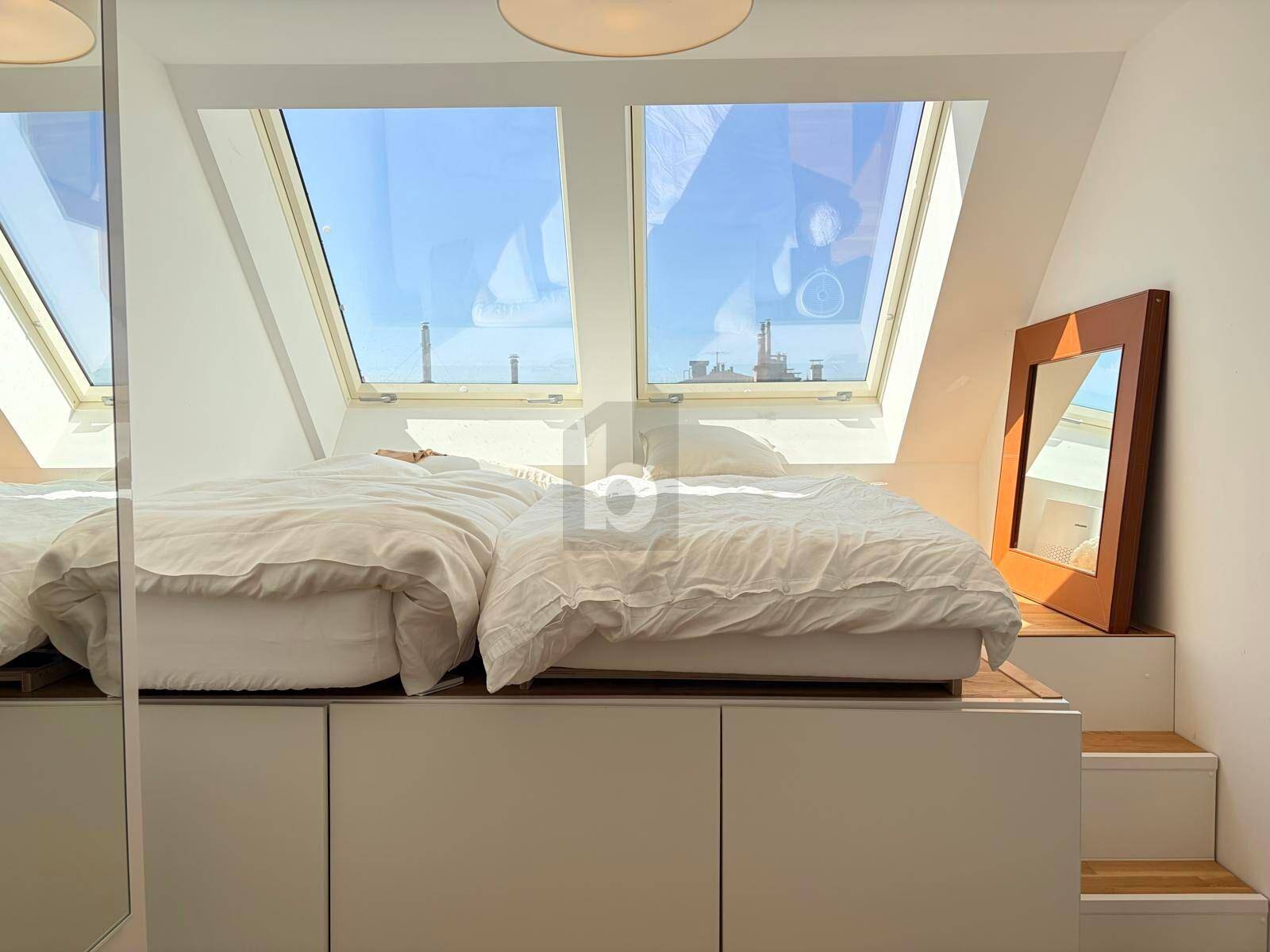 Gemütliches Schlafzimmer im Dachgeschoss mit zwei Betten auf einer erhöhten Plattform und Dachfenstern.