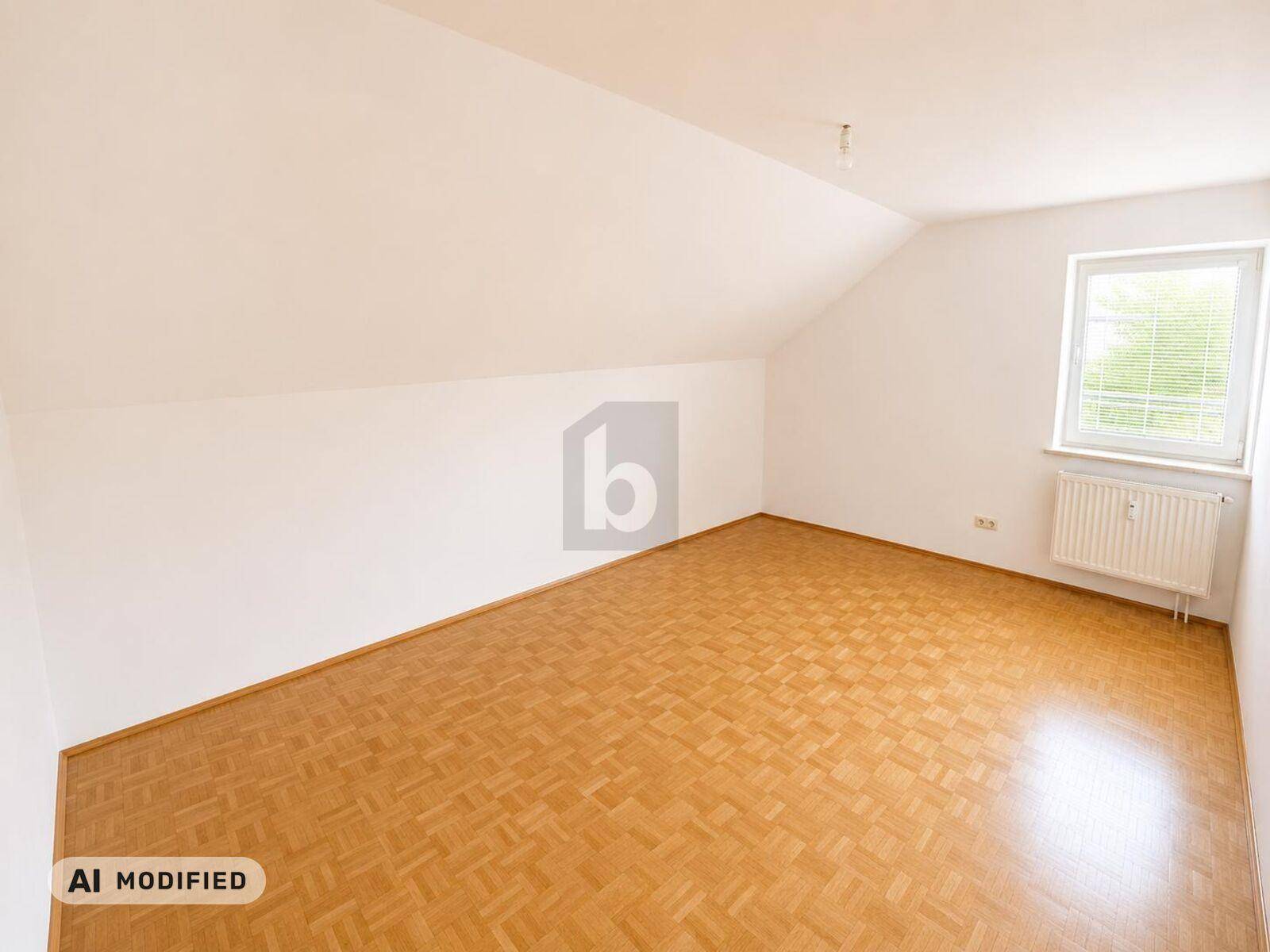 Leeres Zimmer mit Parkettboden, weiß gestrichenen Wänden und Dachschräge.