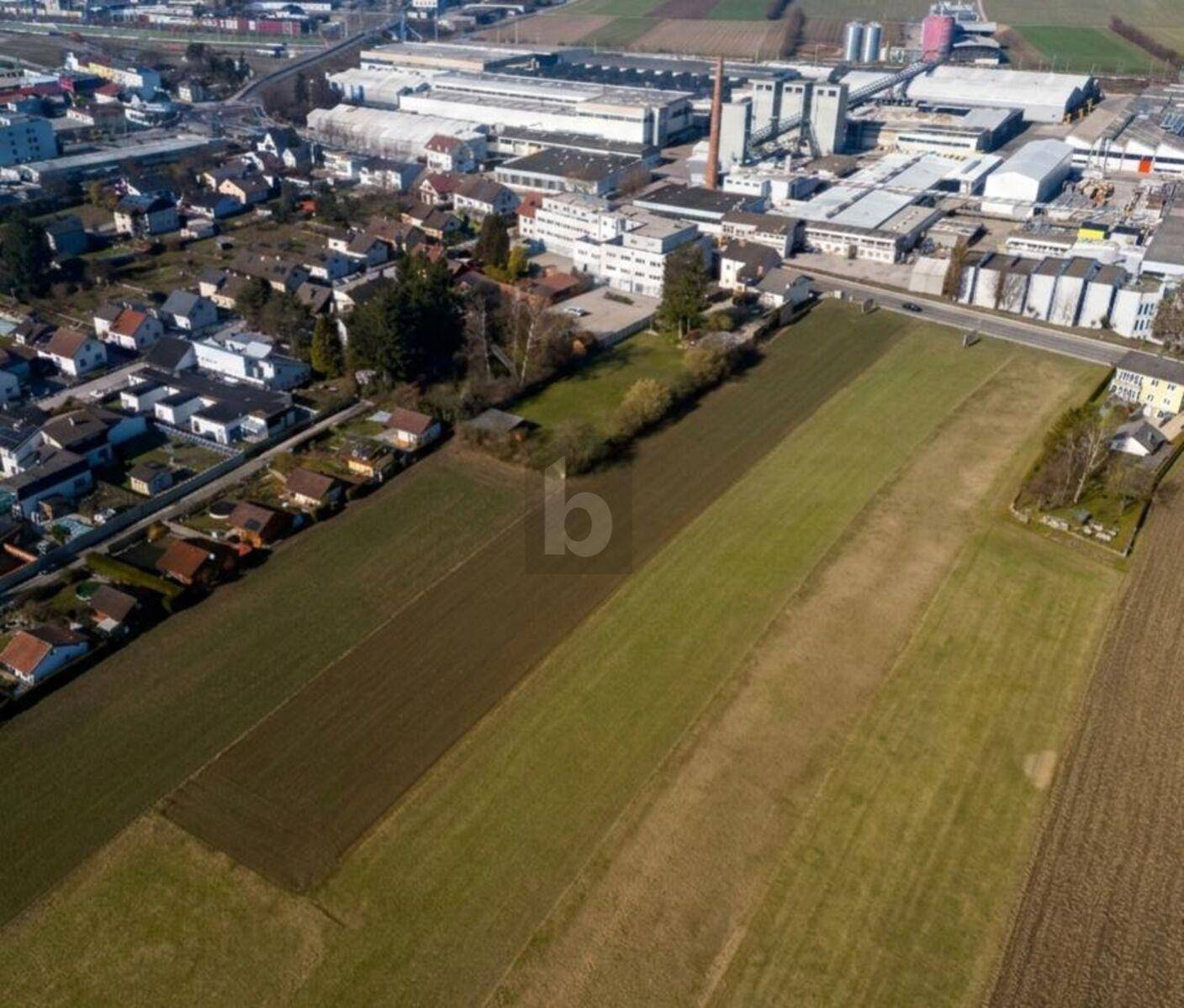 Panoramablick aus der Luft auf Felder, eine Wohnsiedlung und angrenzende Industriegebäude.