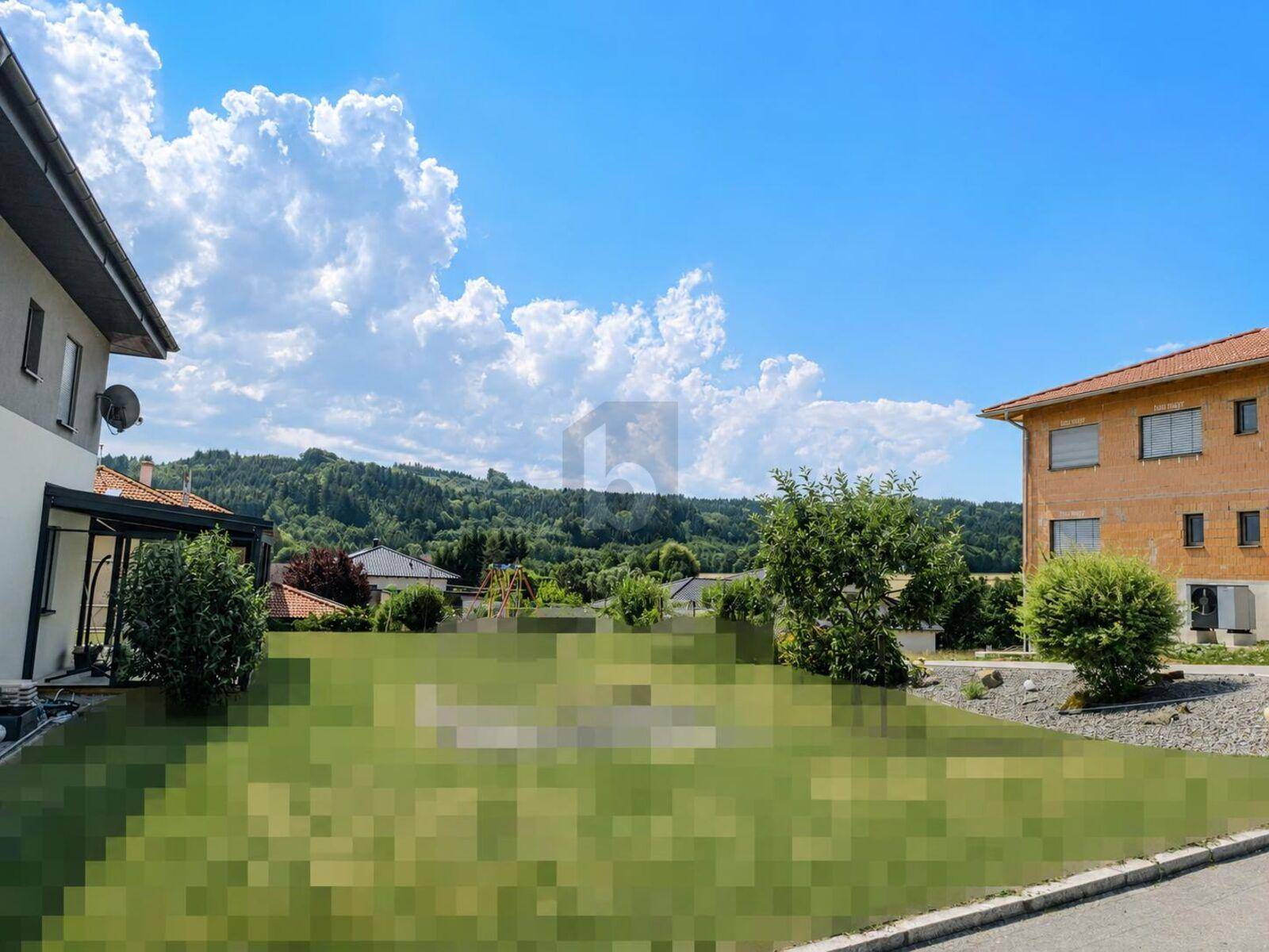 Blick auf eine Wohnsiedlung mit Häusern, einem Spielplatz und grünen Hügeln im Hintergrund.