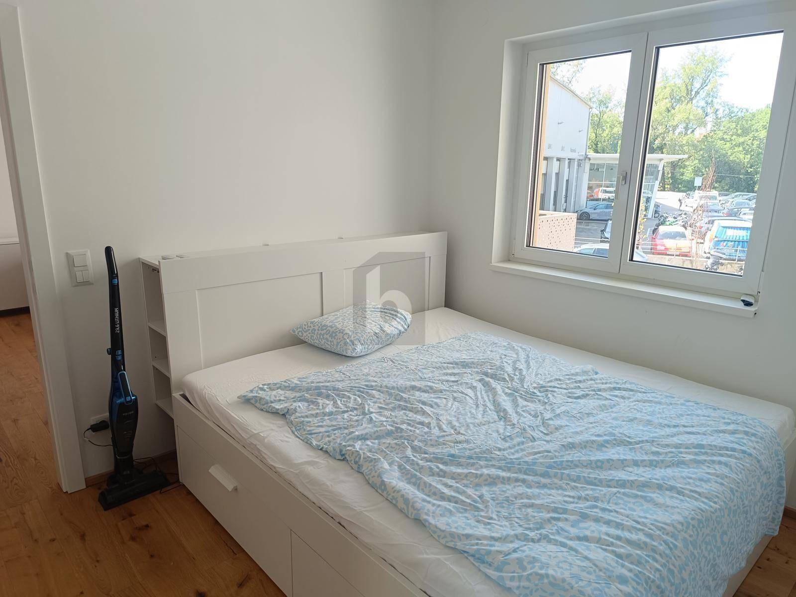 Helles Schlafzimmer mit weißem Bettrahmen, blauem Bettzeug und einem großen Fenster.