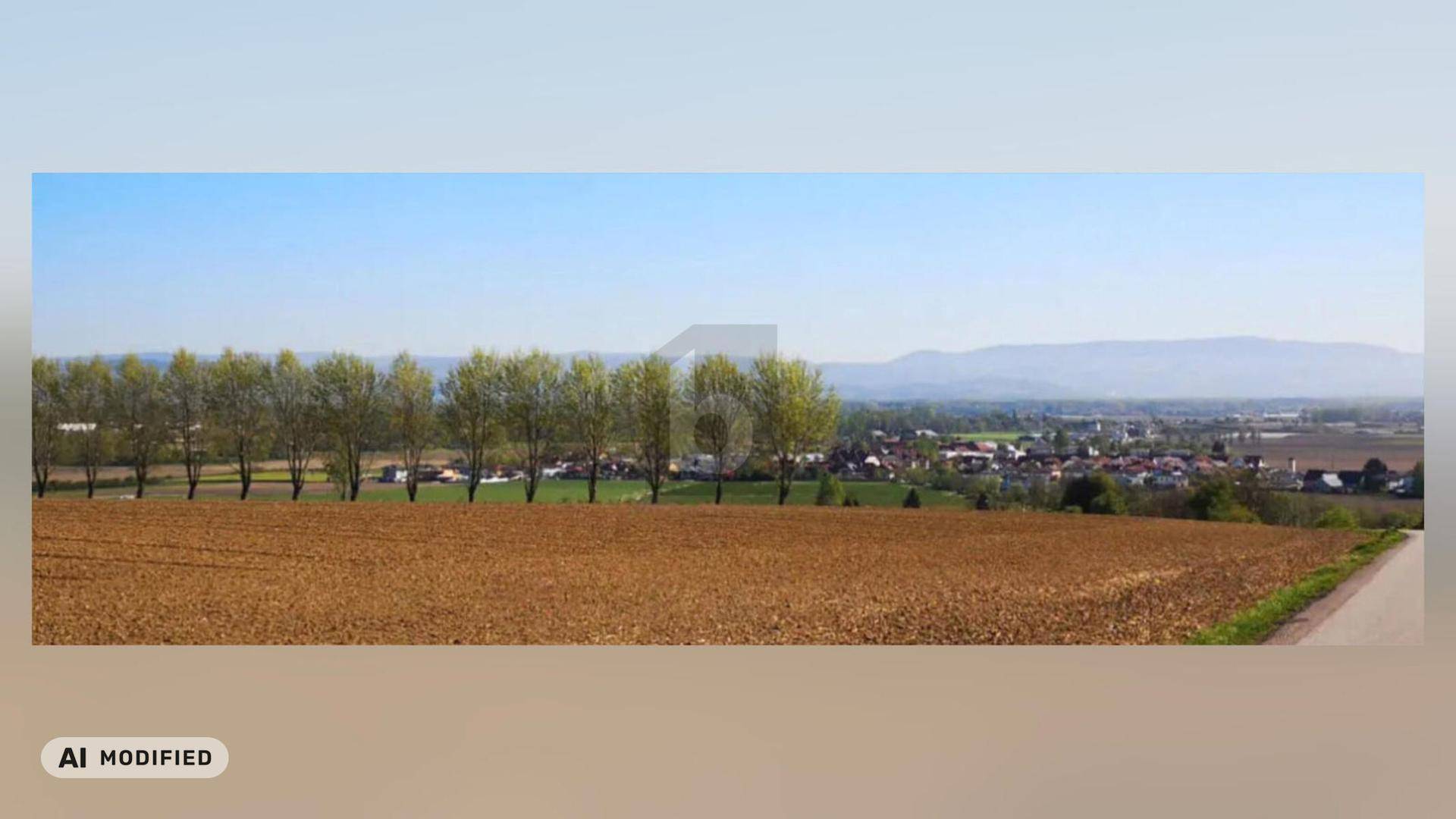 Weitläufige Landschaft mit Feldern, Baumreihe und einem Dorf im Hintergrund unter blauem Himmel.