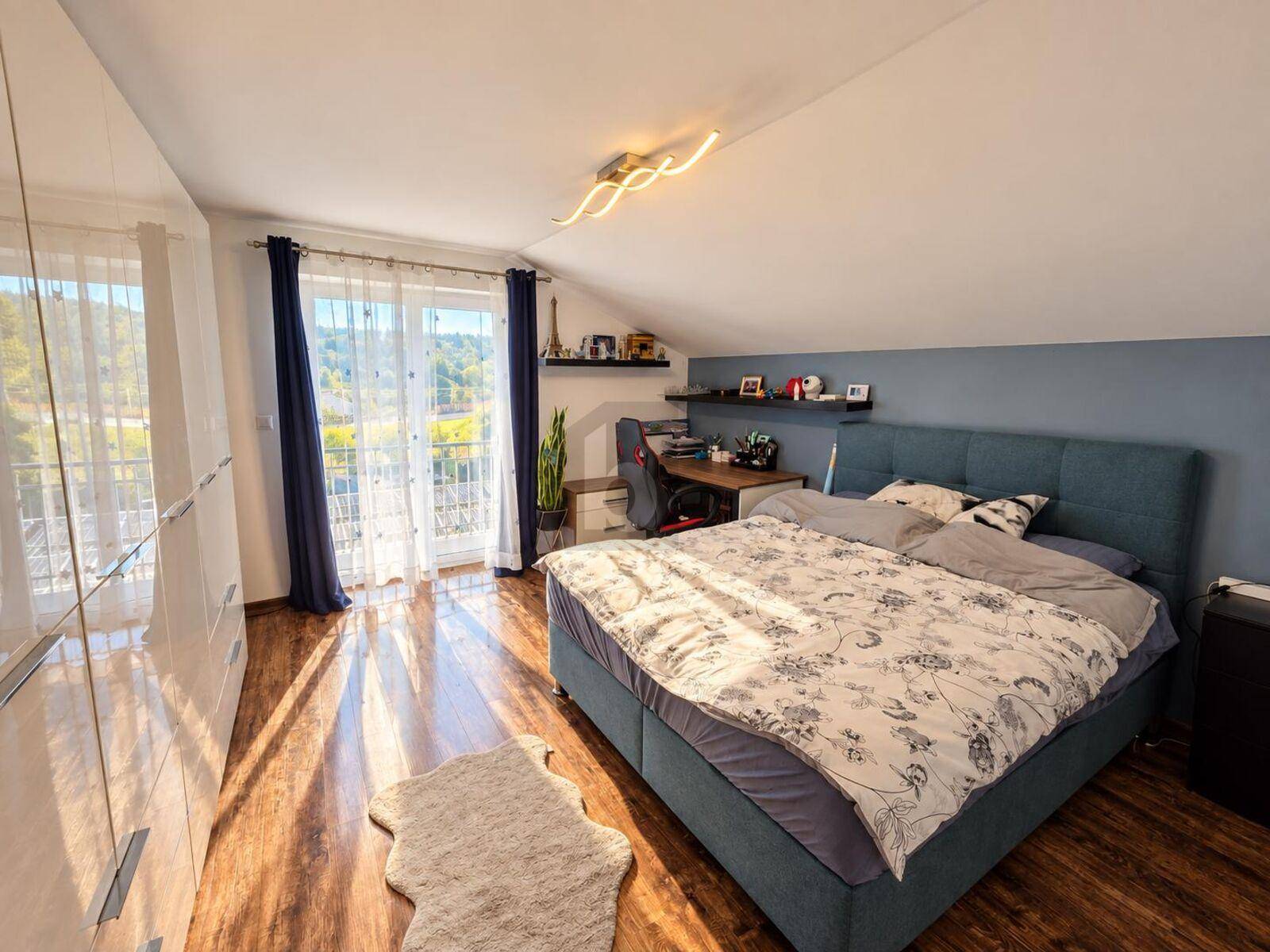 Helles Schlafzimmer mit Holzboden, großem Bett und Zugang zu einem französischen Balkon.