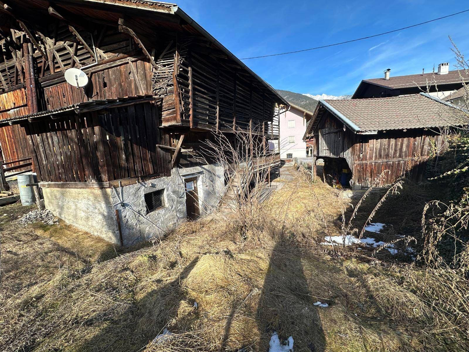 Detailansicht eines alten Holzgebäudes mit verwitterter Fassade und umgebender Vegetation.