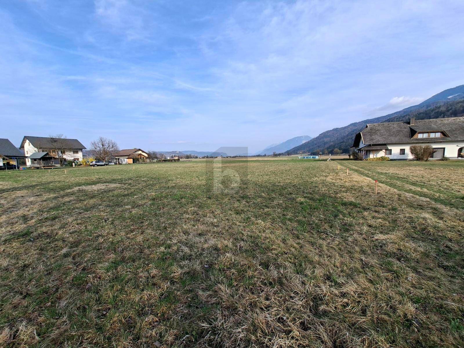 Panoramablick über ein weites Feld mit Bergen und ländlicher Bebauung im Hintergrund.