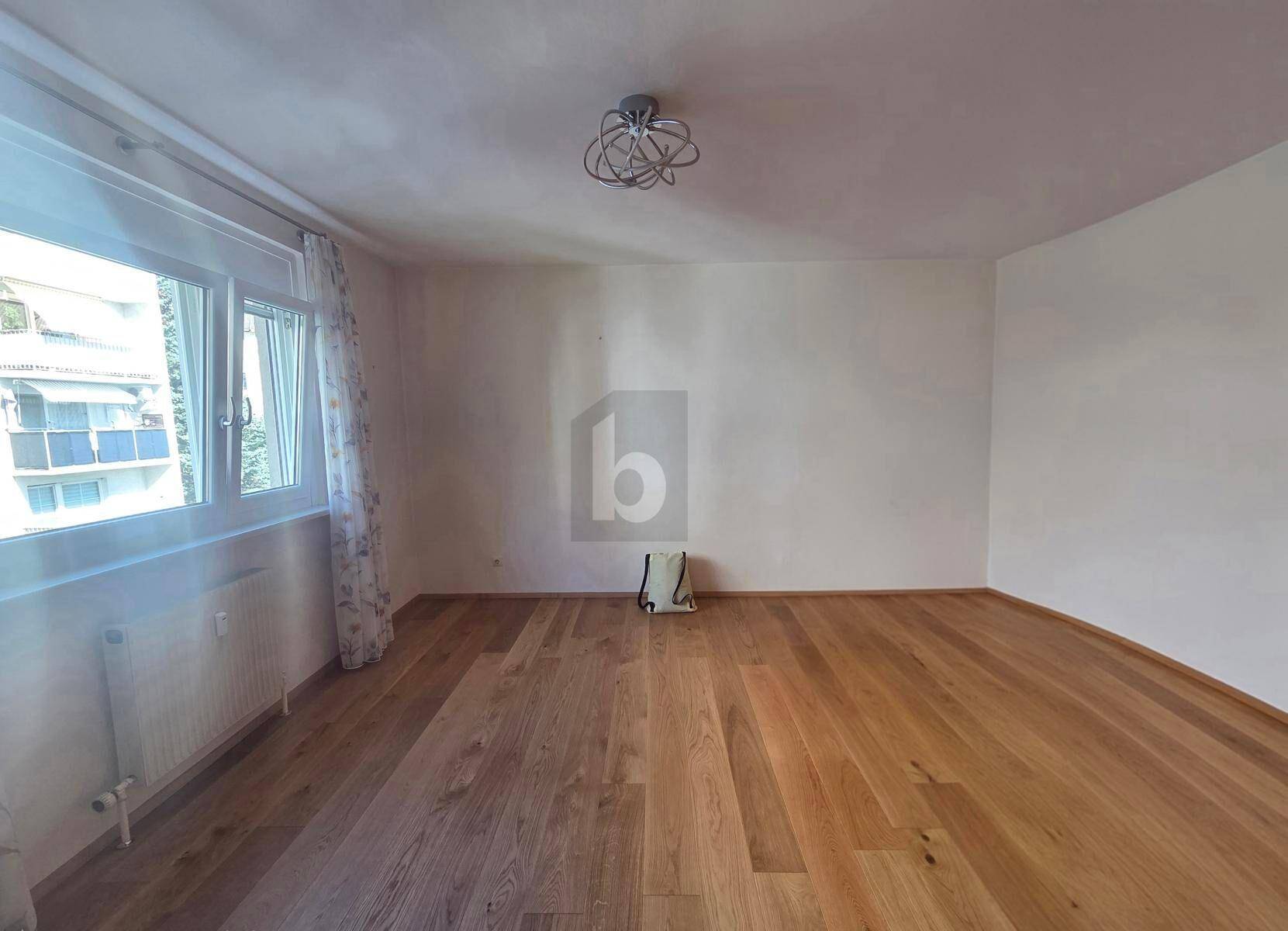 Helles Schlafzimmer mit Holzboden und großen Fenstern, bereit zur individuellen Gestaltung.