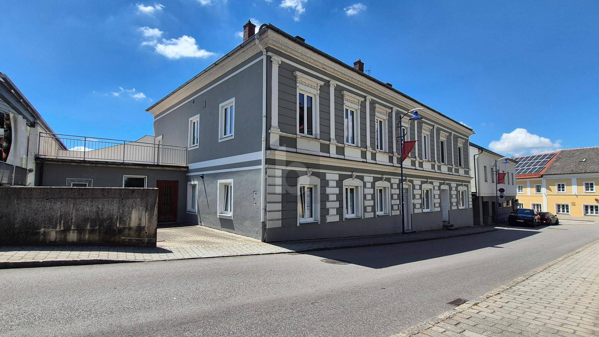Ansicht des historischen Gebäudes mit einer kleinen Terrasse im oberen Bereich und blauer Himmel.
