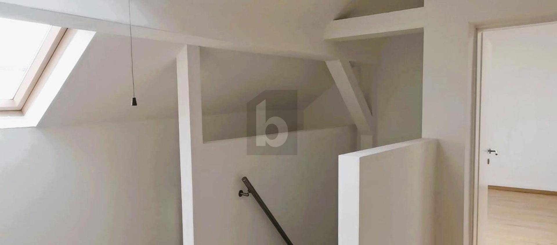 Heller Treppenbereich im Dachgeschoss mit Dachfenster und schrägen Wänden.