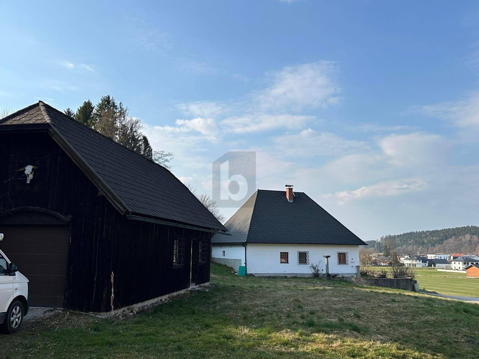 Blick auf das weiße Haus und ein dunkles Holzgebäude auf einem weitläufigen Grundstück.