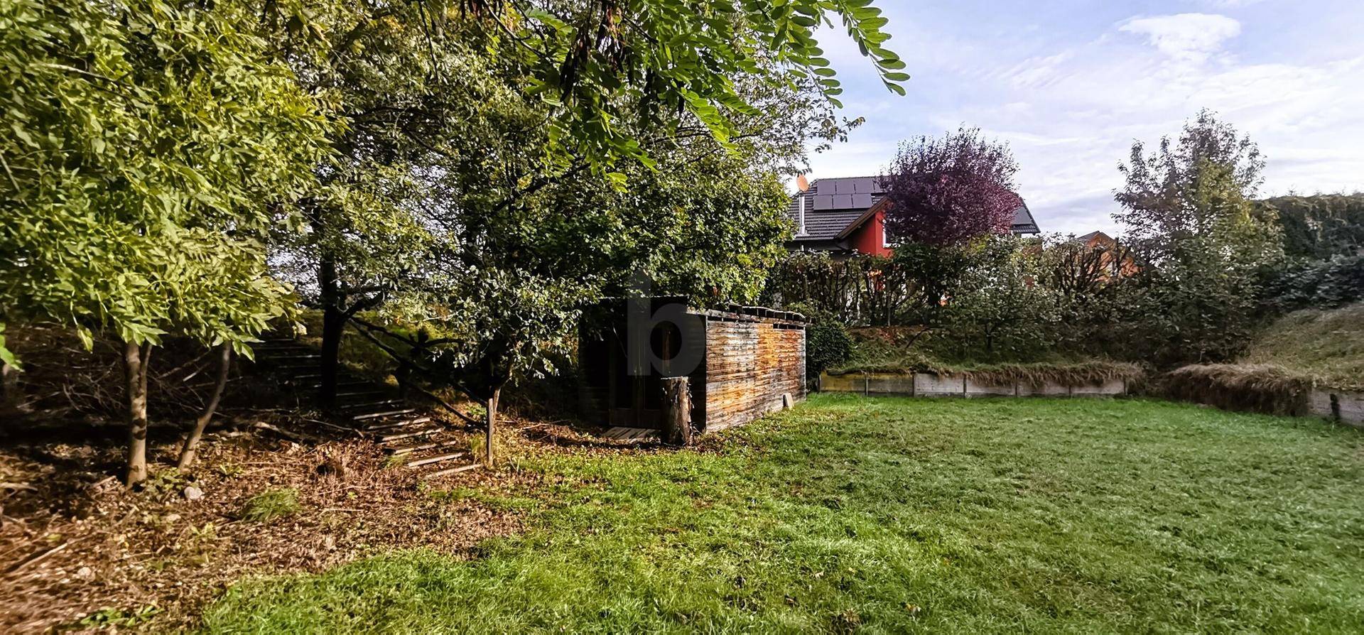 Gepflegter Garten mit Rasen, einem Holzschuppen und einem Haus mit Photovoltaikanlage im Hintergrund.
