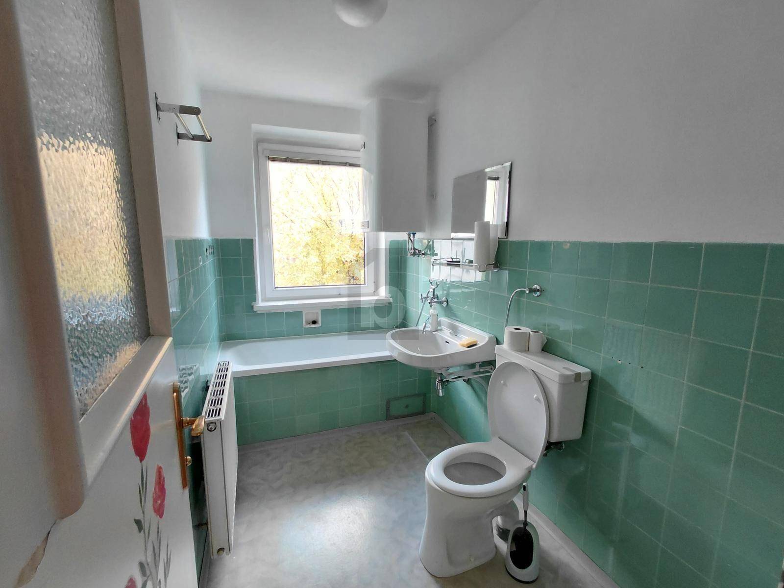 Badezimmer mit mintgrünen Fliesen, Badewanne, Waschbecken und Fenster.