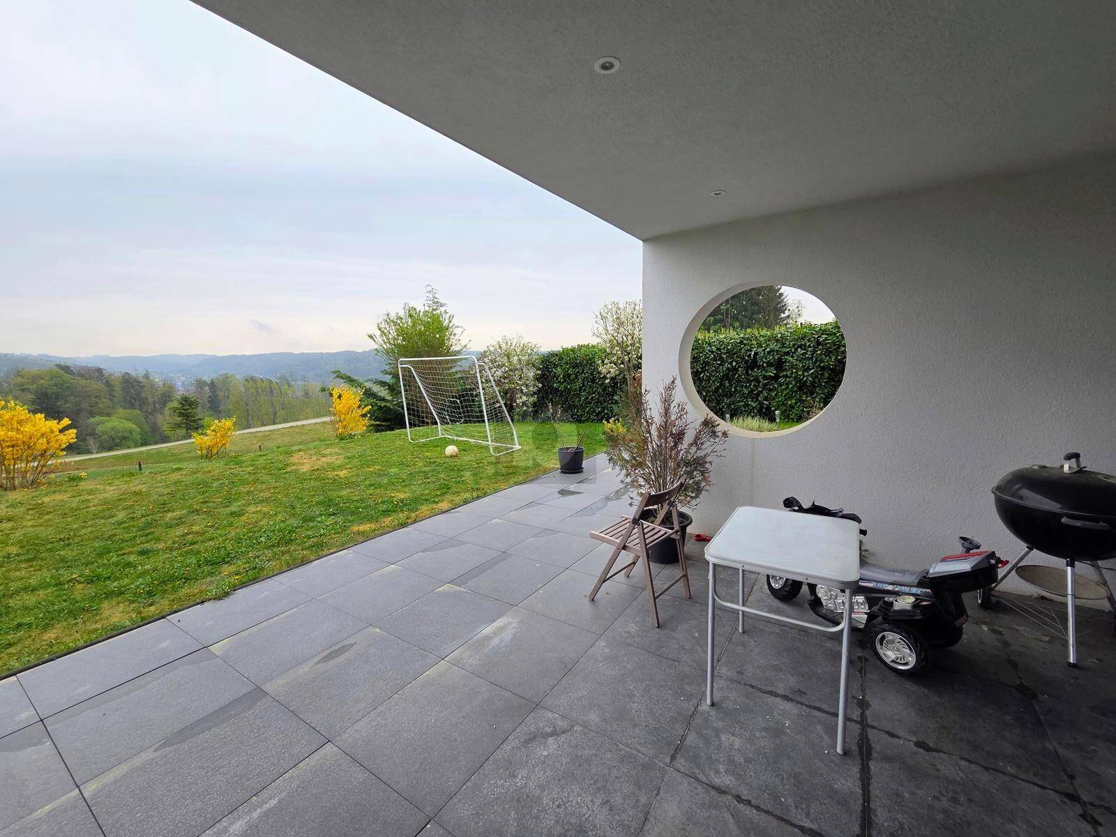 Große gepflasterte Terrasse mit Grillbereich und weitem Blick über den grünen Garten und die Landschaft.