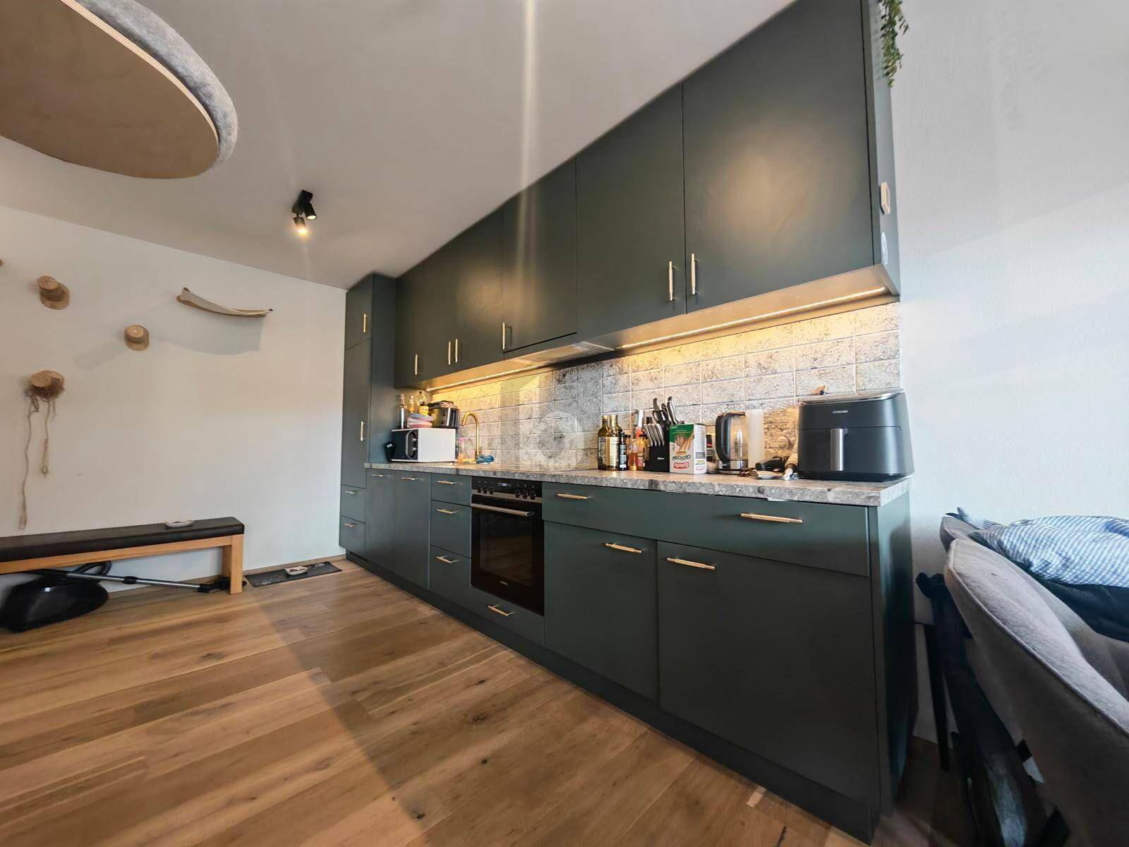 Moderne Küche mit dunkelgrünen Schränken, Holzfußboden und integrierten Geräten.