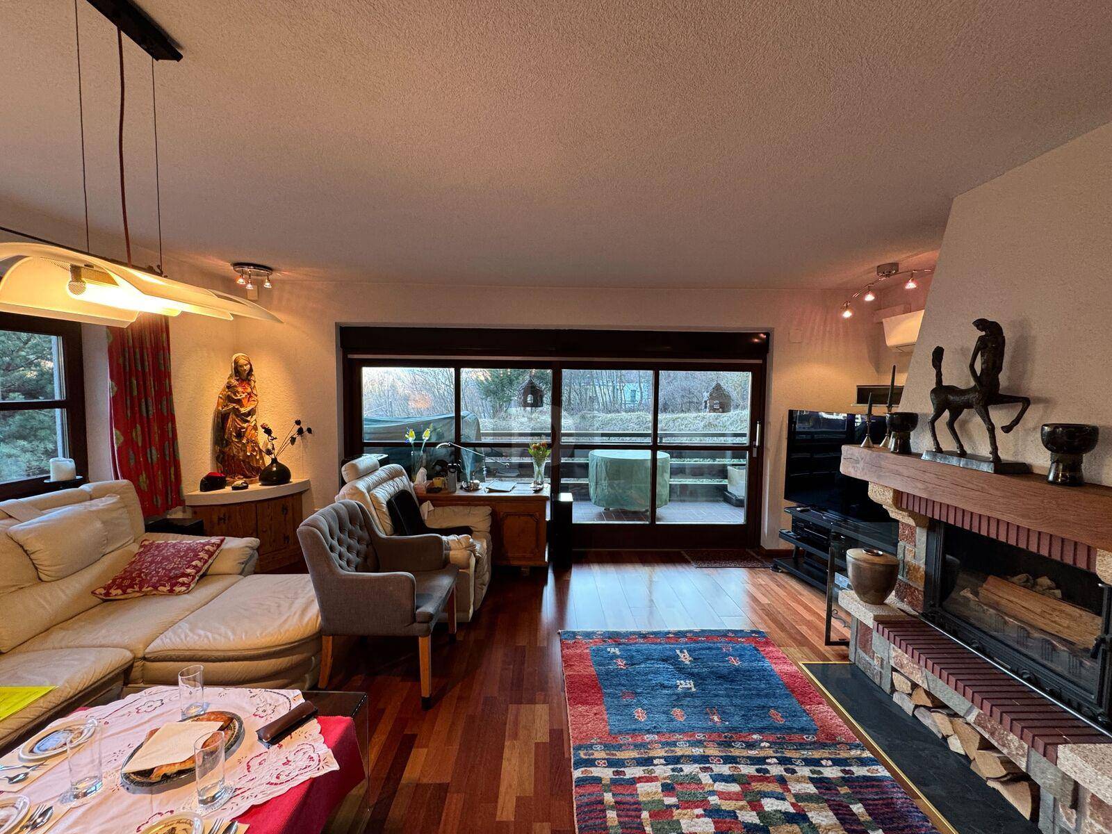 Helles Wohnzimmer mit Kamin, Holzboden und Zugang zu einem Balkon.