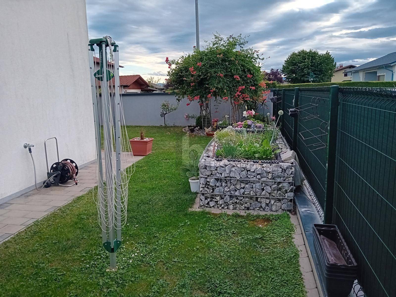 Gepflegter Gartenbereich mit Rasenfläche, Gabionen-Hochbeet und Wäschespinne.