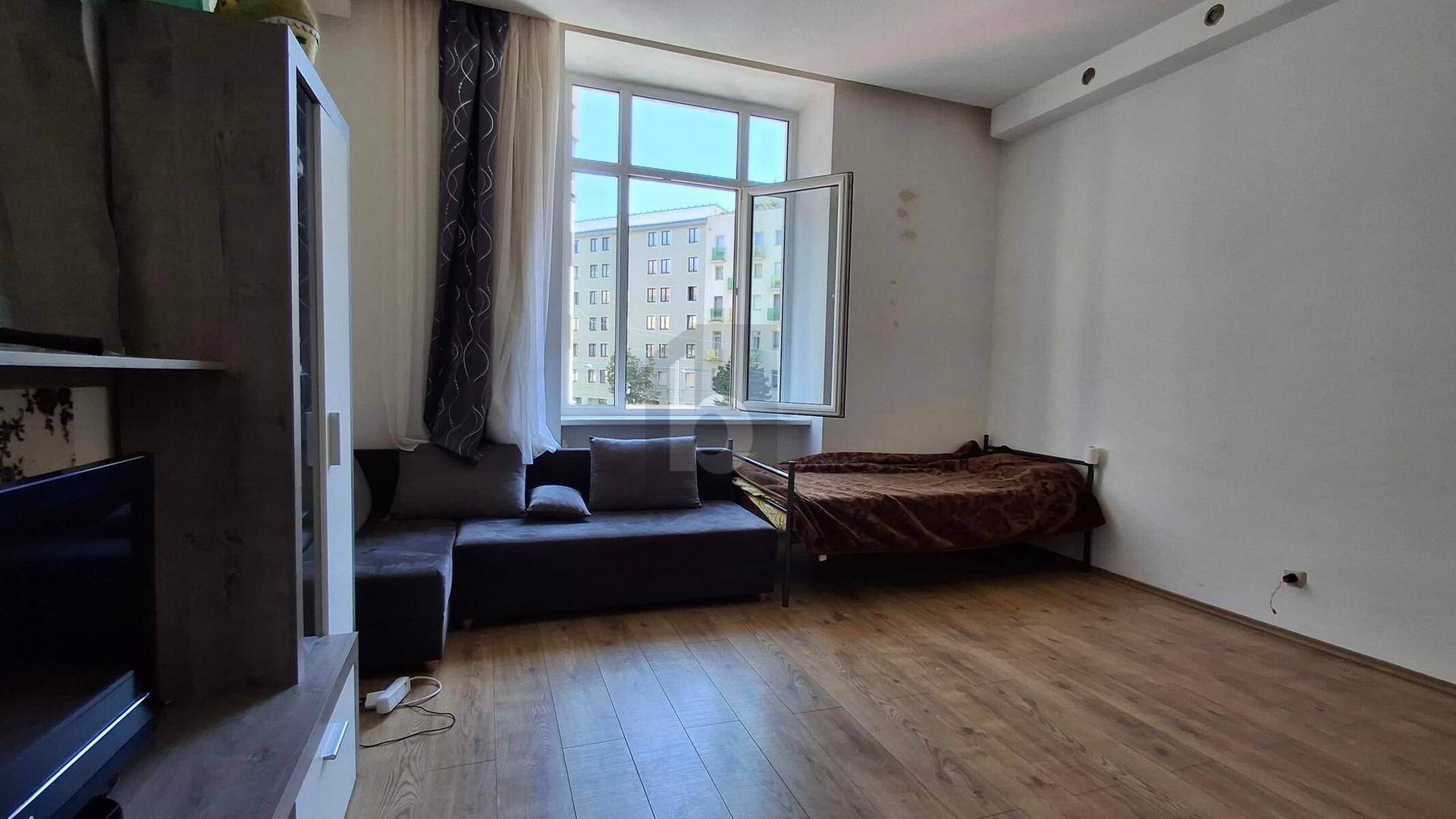 Helles Zimmer mit Holzboden, Sofa und Bett, bietet Blick auf die umliegenden Gebäude.