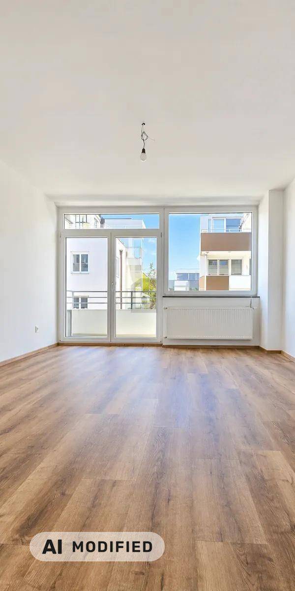 Heller, leerer Raum mit Holzboden und großen Fenstern, die Zugang zu einem Balkon bieten.
