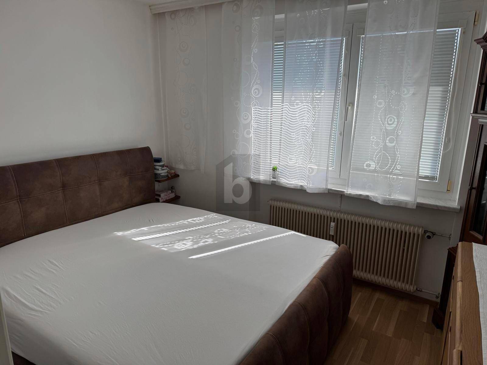 Gemütliches Schlafzimmer mit Doppelbett, Parkettboden und Fenster mit Jalousien.