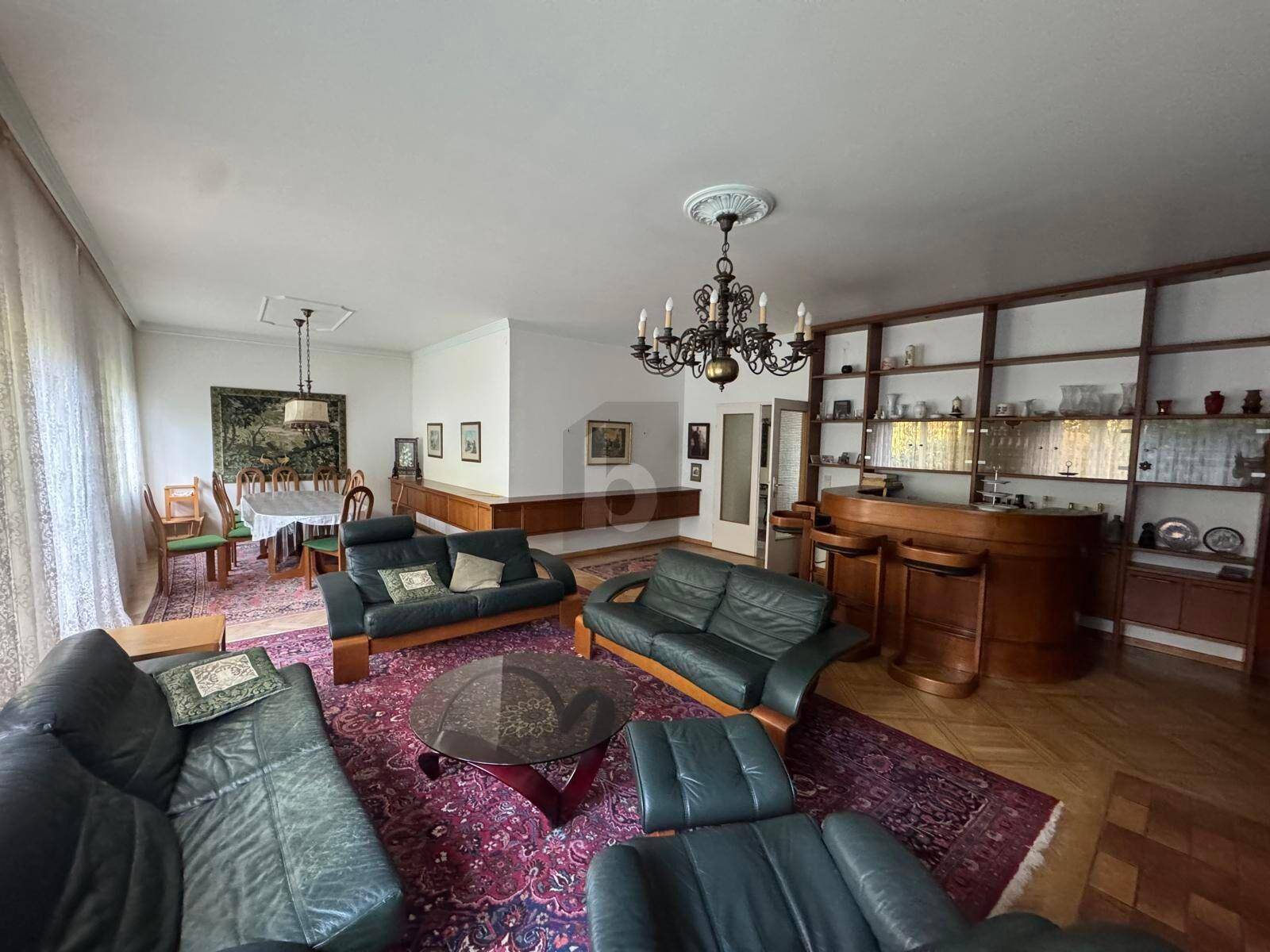 Großzügiger Wohn- und Essbereich mit dunklen Ledersofas, Parkettboden und Kamin.