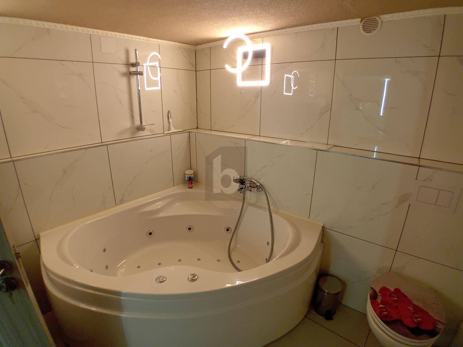 Badezimmer mit einer Eck-Whirlpool-Badewanne und hellen Fliesen an den Wänden.
