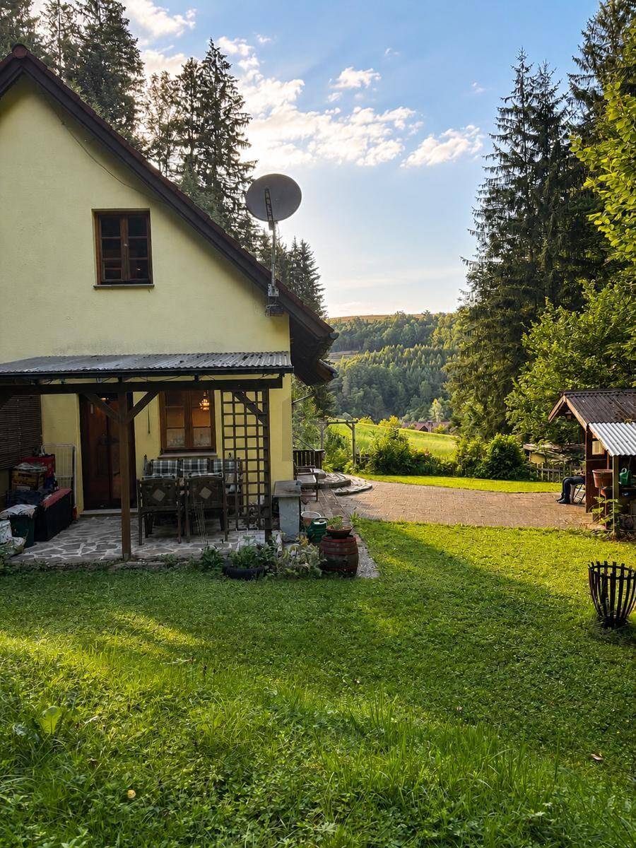 Sonniges Landhaus mit überdachter Terrasse und weitem Blick über grüne Hügel und Wälder.