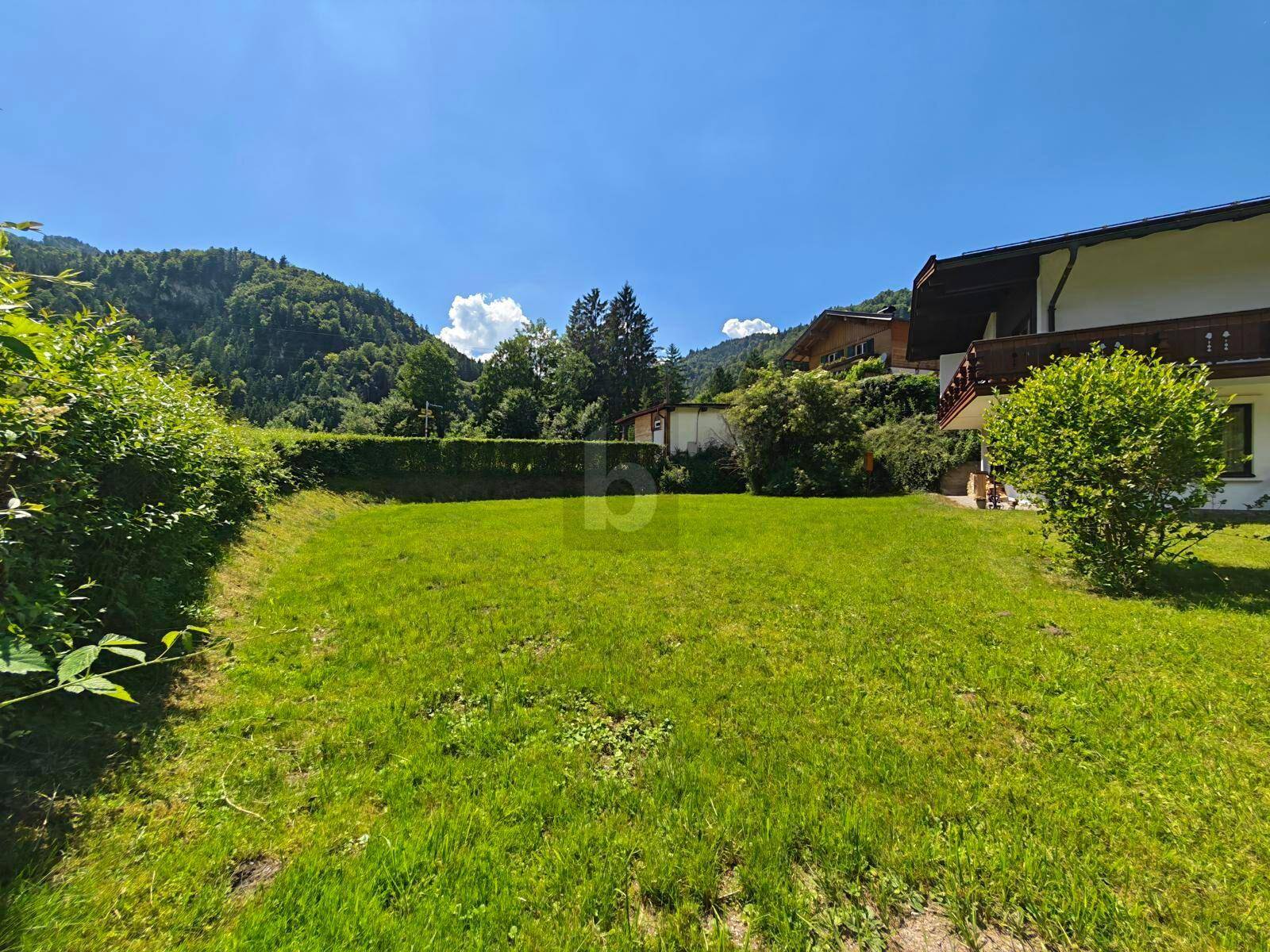 Gepflegter Gartenbereich mit Rasenfläche, umgeben von Hecken und einem schönen Bergblick.