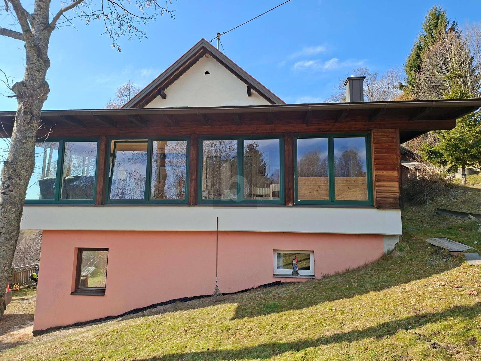 Seitenansicht des Hauses mit großer Fensterfront des Wintergartens und Hanglage im Sonnenlicht.