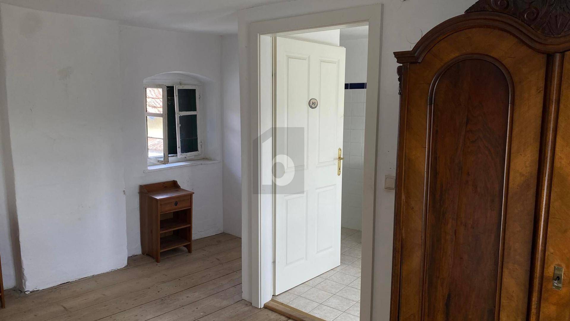 Schlafzimmer mit Holzdielenboden, antikem Kleiderschrank und kleinem Fenster.