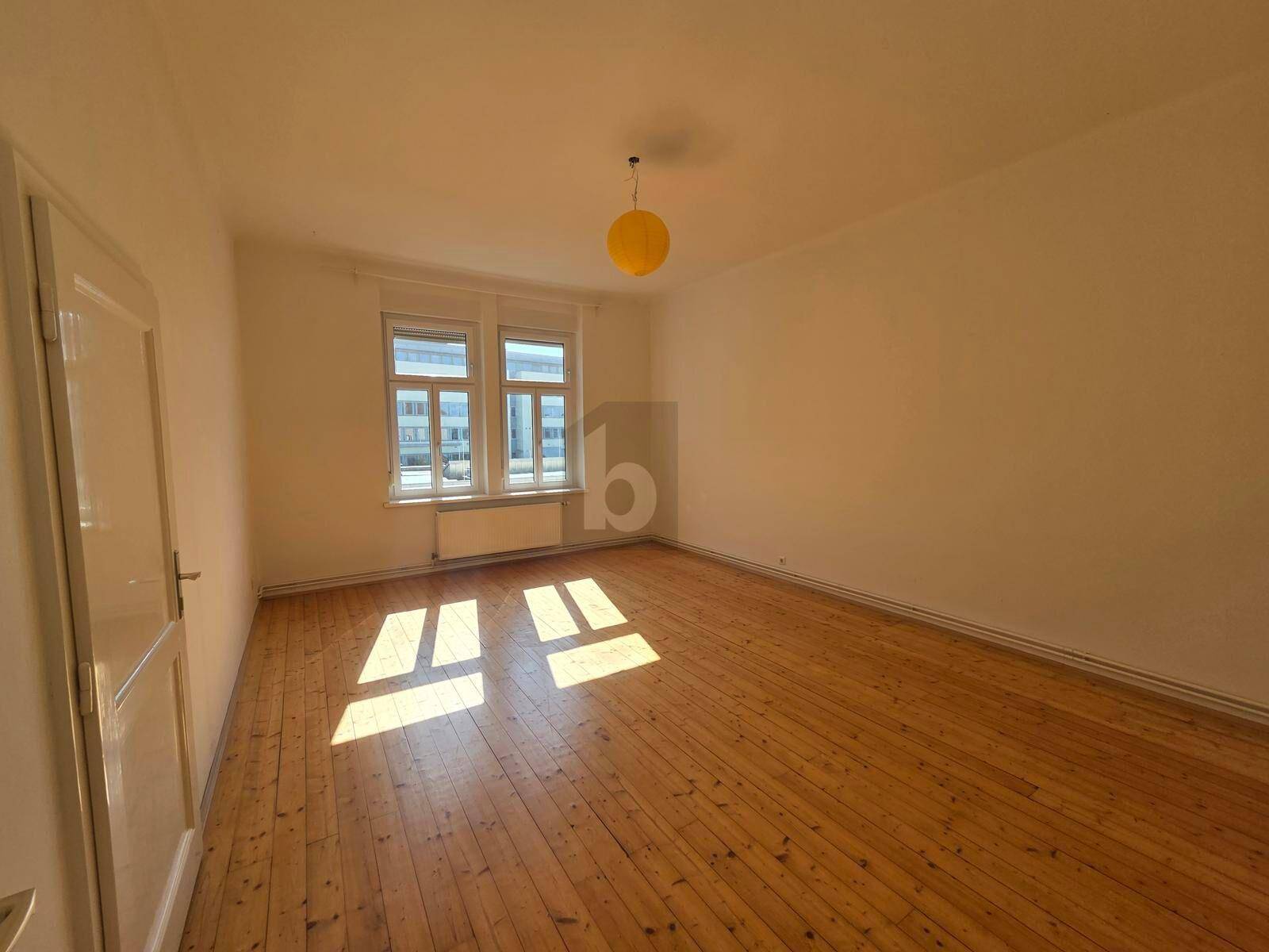 Helles Schlafzimmer mit Holzdielenboden, großen Fenstern und einem gelben Deckenlicht.