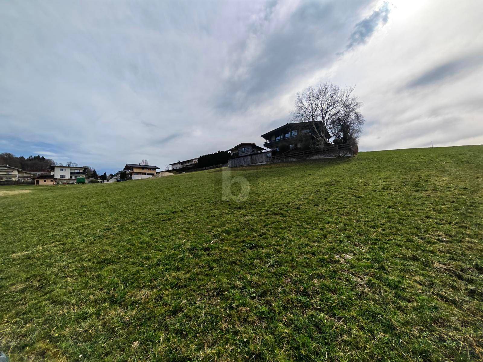 Grüner Hügel mit Häusern am Horizont unter einem bewölkten Himmel.