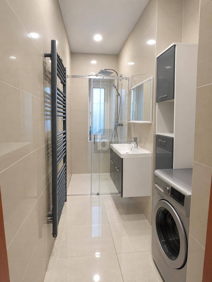 Modernes Badezimmer mit beigefarbenen Fliesen, ebenerdiger Dusche und Waschmaschine.